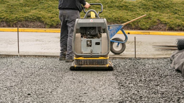 Contractor using plate compactor equipment on crushed gravel base for brick paver installation